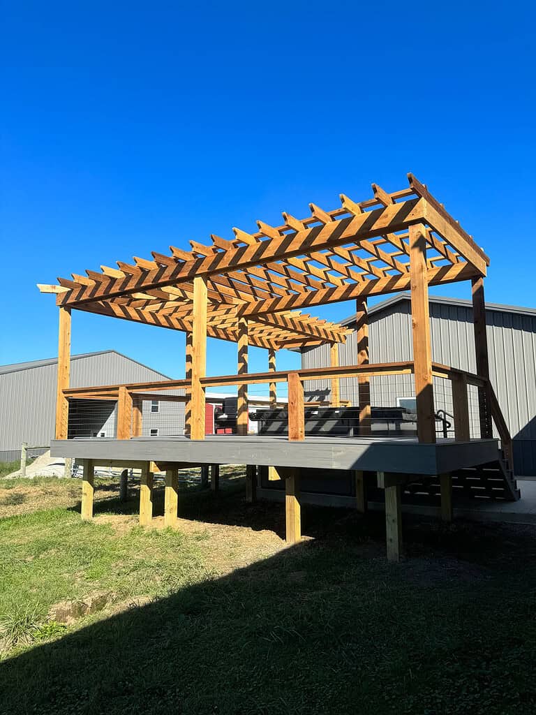 Solid wood pergola outdoor structure with a slatted roof on a raised deck in a backyard, designed for outdoor entertaining and shade, built by McFarland Outdoors.
