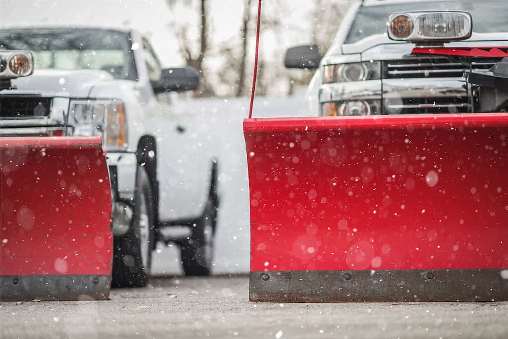 Snow plows attached to trucks preparing for winter snow removal, emphasizing outdoor equipment and snow management services.