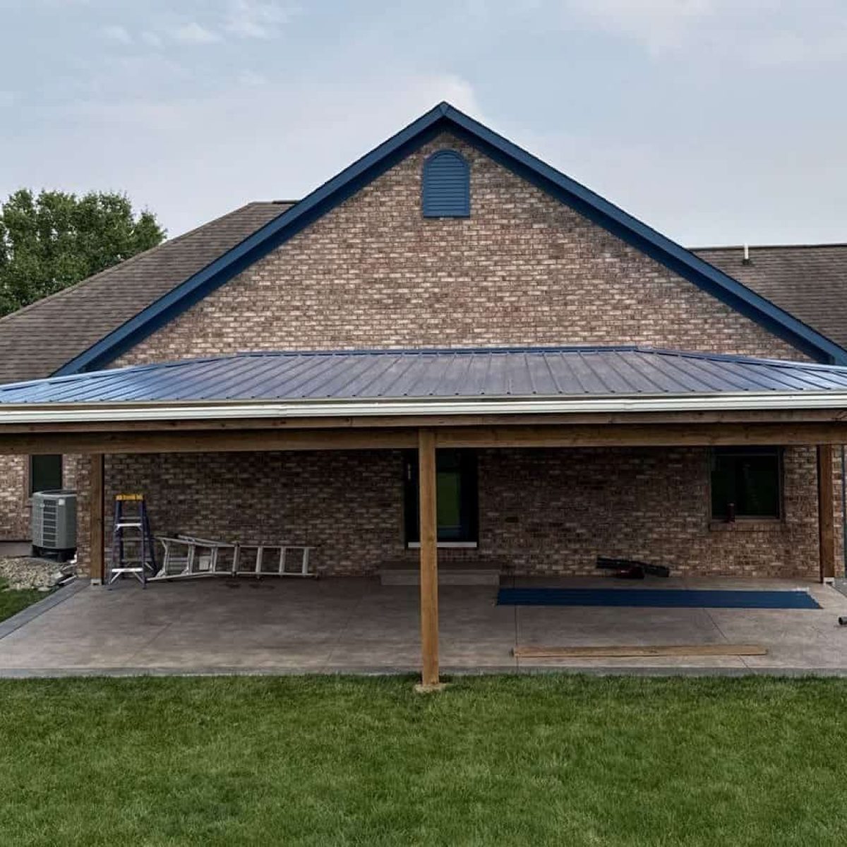 Custom screened porch construction with a metal roof, attached to a brick house, surrounded by a lush green lawn.