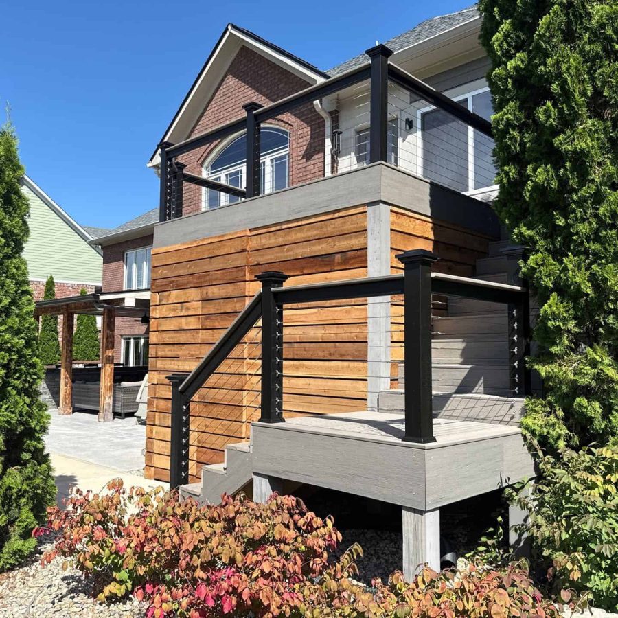 Modern backyard deck with wooden and composite materials, black metal railing, surrounded by lush greenery, perfect for outdoor entertaining and enjoying nature.